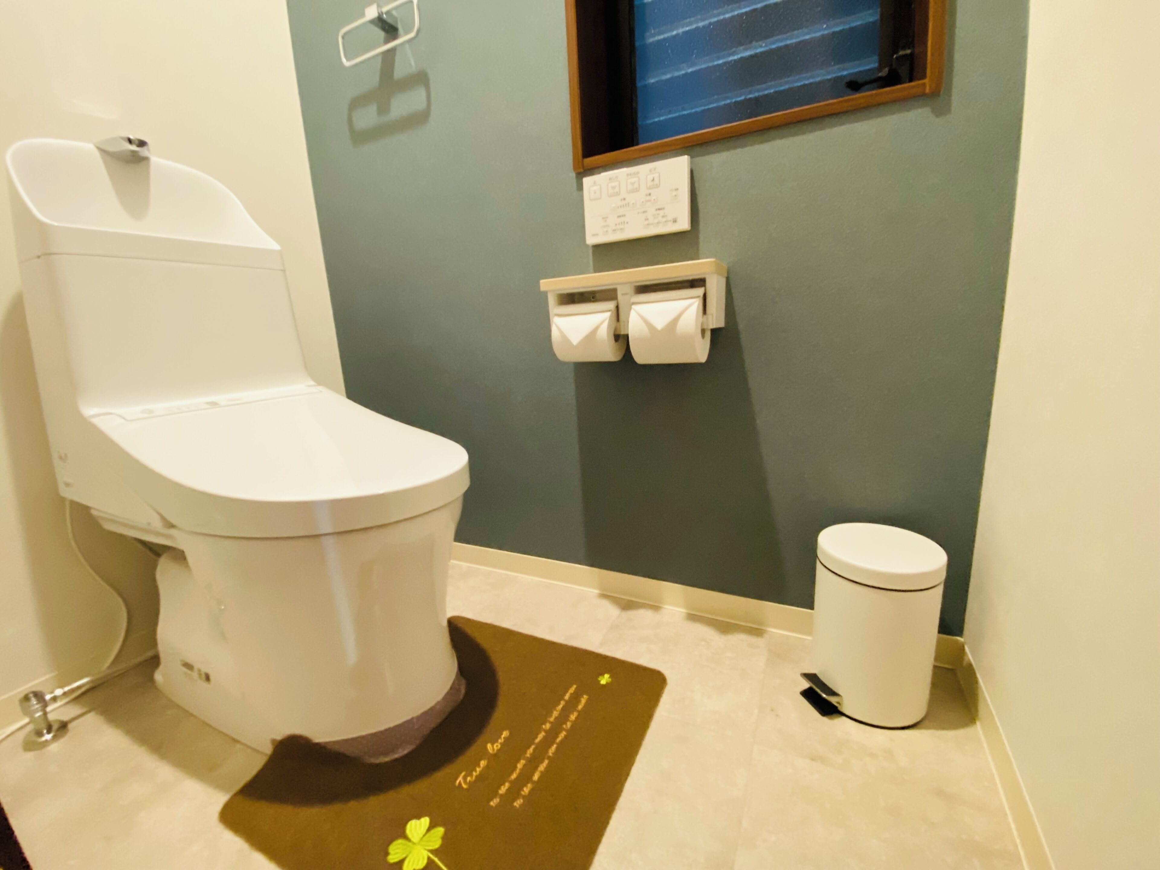 Une salle de bain équipée de toilettes, d’une poubelle, d’un distributeur de serviettes et d’une petite fenêtre.