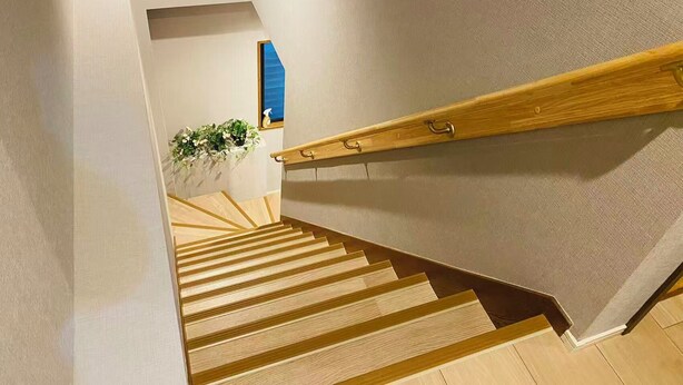Un escalier en bois avec une rampe, une plante en pot et un objet bleu accroché au mur.