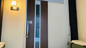 Une porte coulissante avec une plaque portant l’inscription « Villa Kenzo », un luminaire fixé au mur et une poubelle.