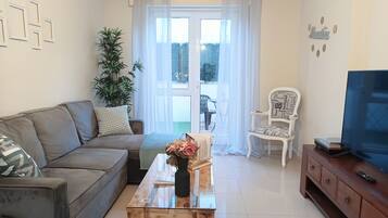 A living room with a sofa, a coffee table with flowers, a TV on a cabinet, and a chair with a nameplate.