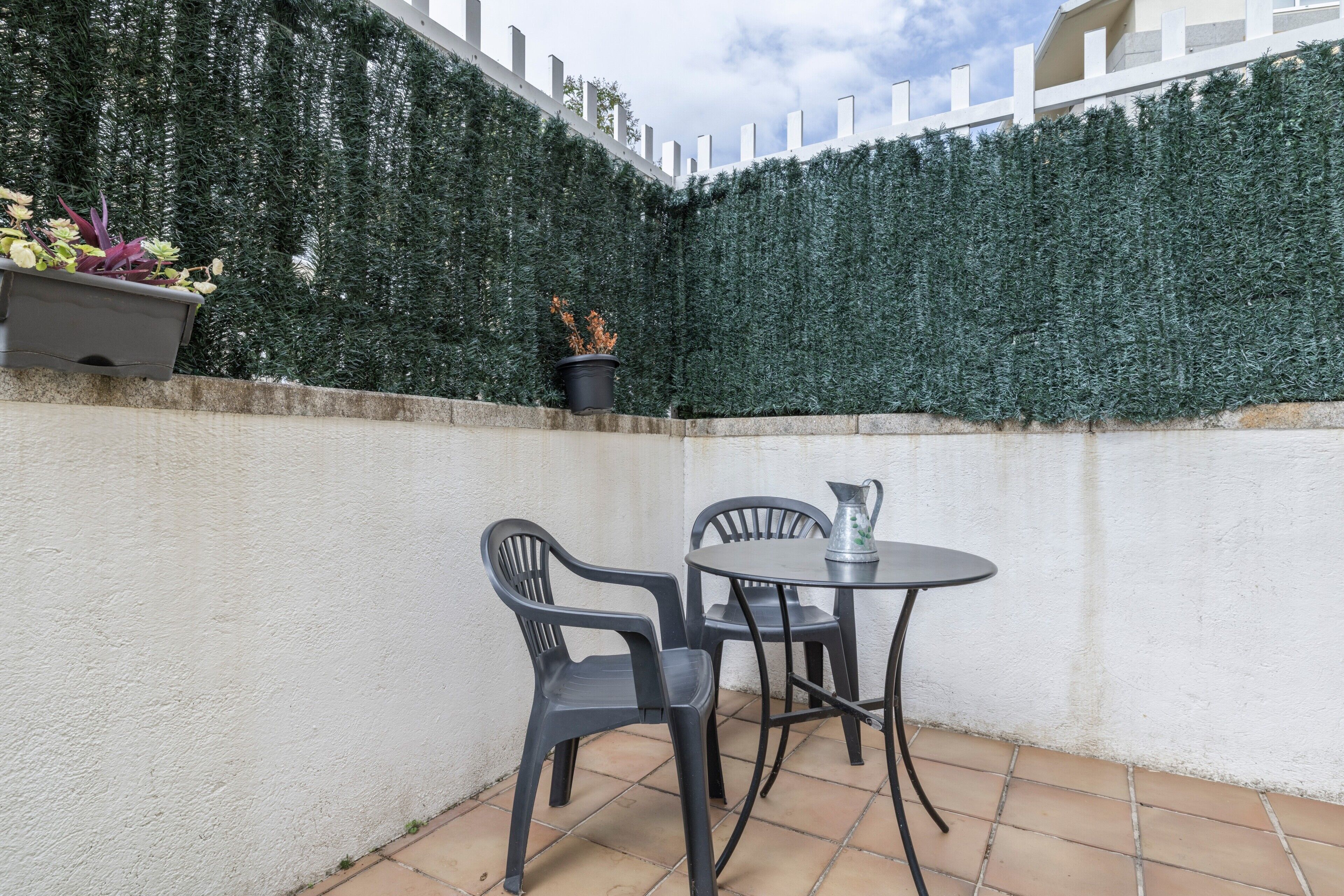 Ein Terrassenbereich mit Tisch und Stühlen, einem Blumentopf und einem weißen Zaun.