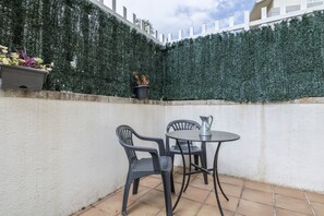 A patio area with a table and chairs, a potted plant, and a white fence.