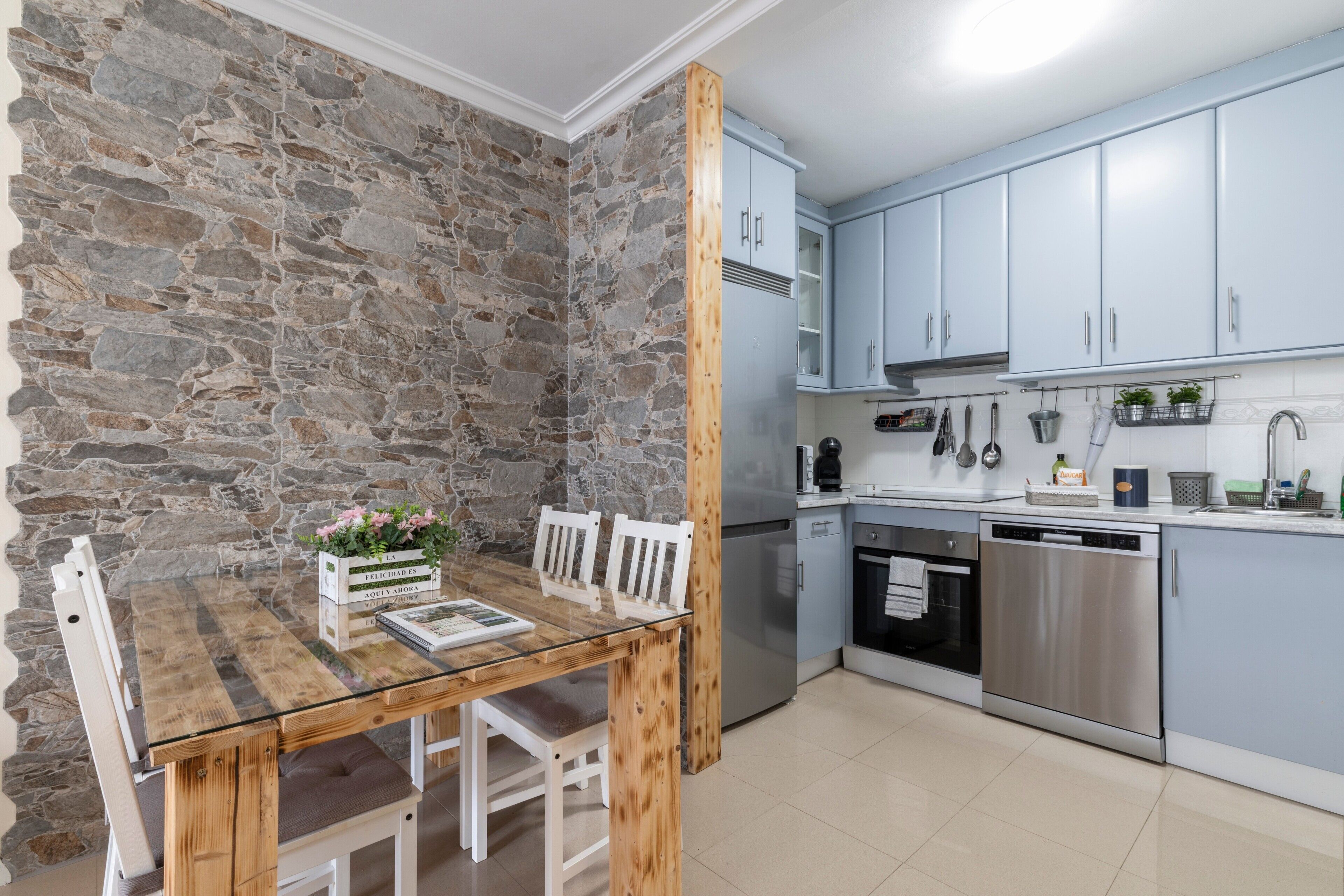 Una cocina moderna con armarios azul claro, pared de piedra y una mesa de comedor de madera con sillas.