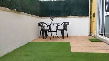 Ein kleiner Patio-Bereich mit Kunstgrras, einem Tisch und zwei Stühlen, begrenzt durch eine Hecke.