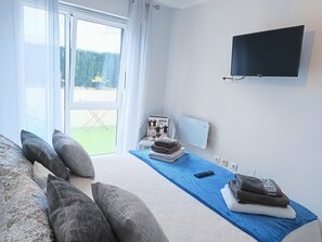 Een hotelkamer met een bed, een televisie, een raam met gordijnen, een stoel en een klein tafeltje met handdoeken.