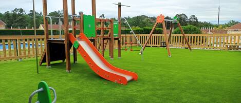 Un parque infantil con tobogán, columpios y una estructura para escalar.