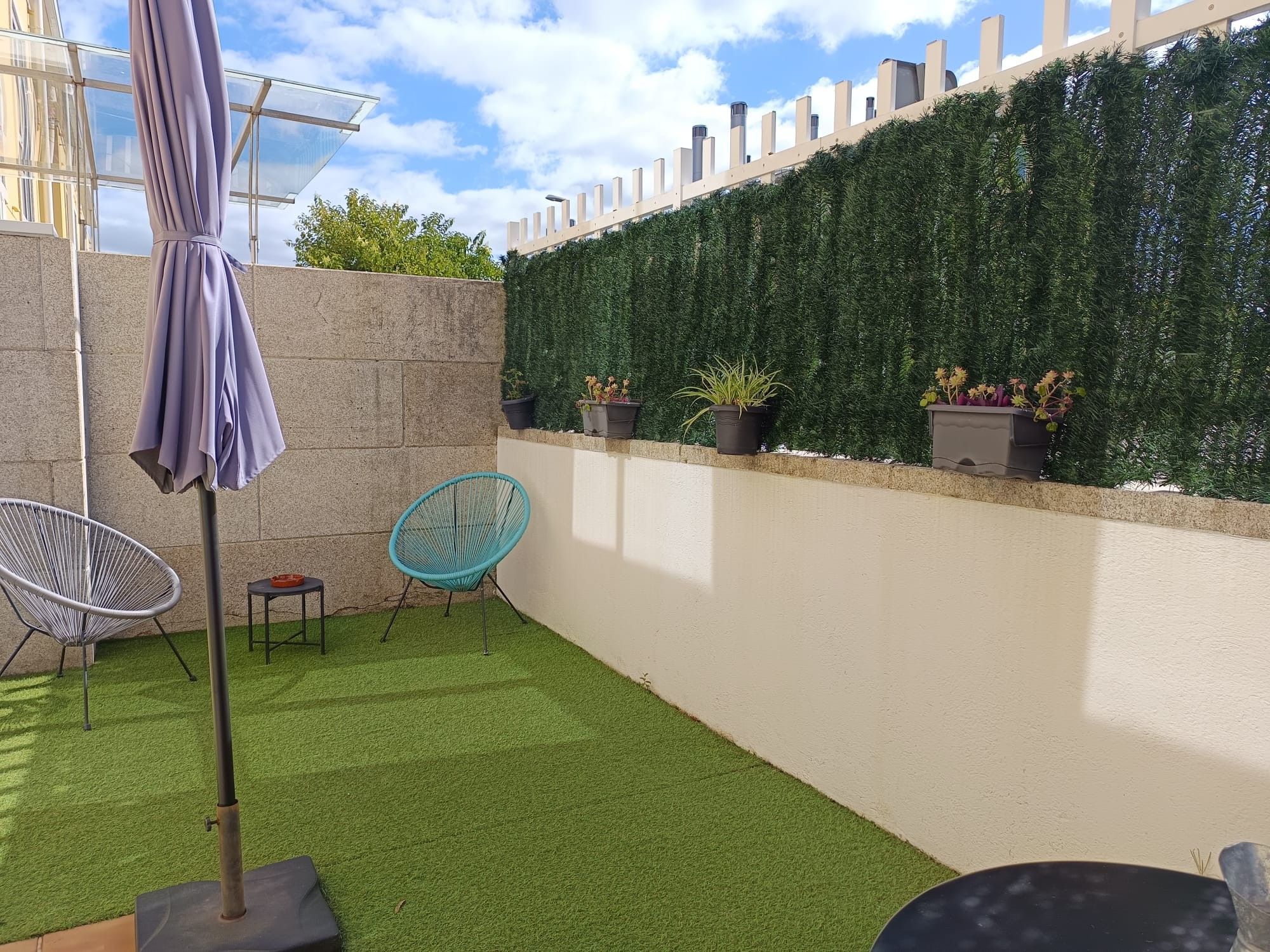 Un patio con césped artificial, un espacio de descanso y una pared con plantas en macetas.