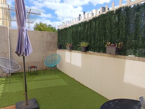 Un patio con césped artificial, un espacio de descanso y una pared con plantas en macetas.
