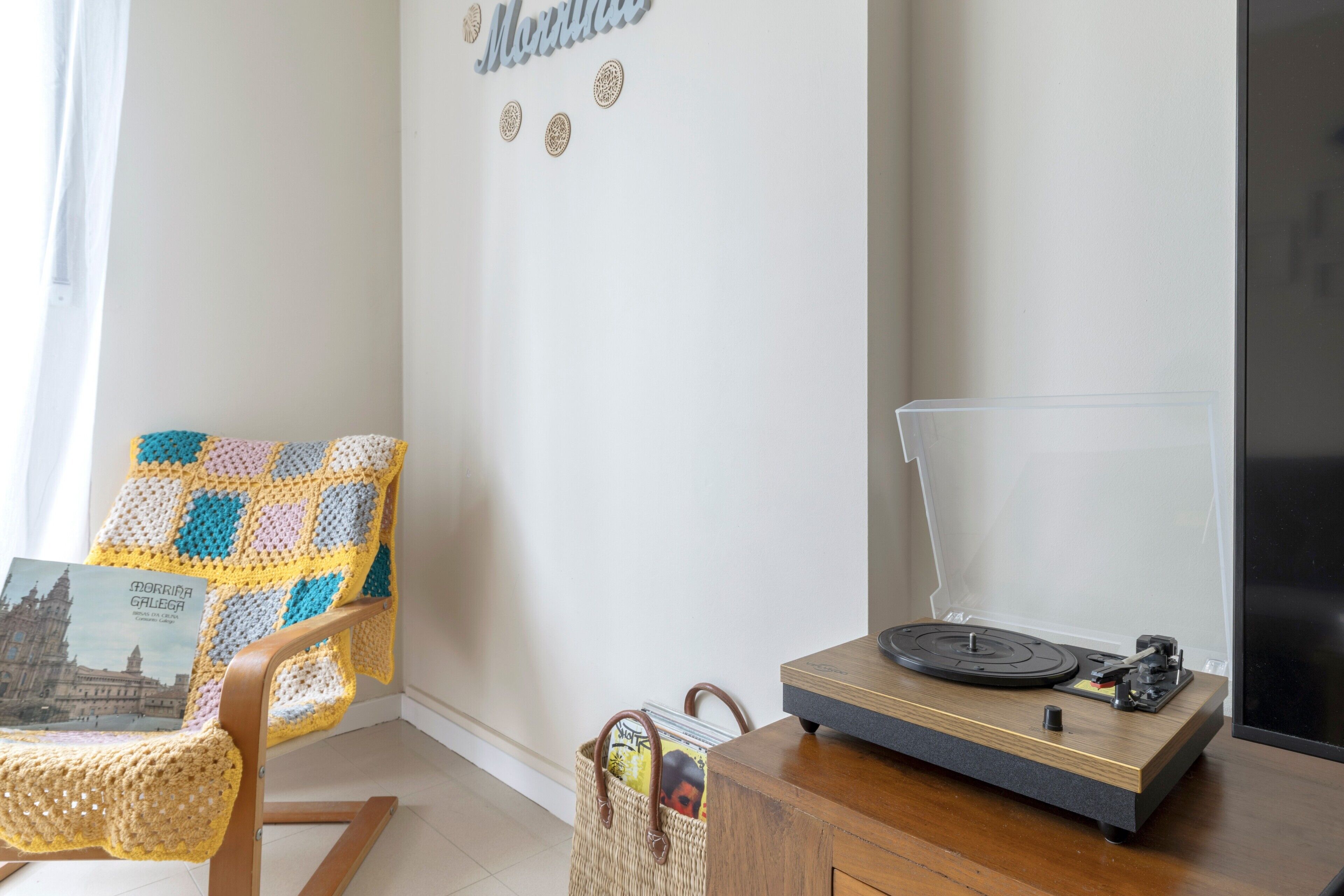 Una habitación acogedora con una silla de madera, una manta de crochet, un tocadiscos y una pared decorada con objetos.