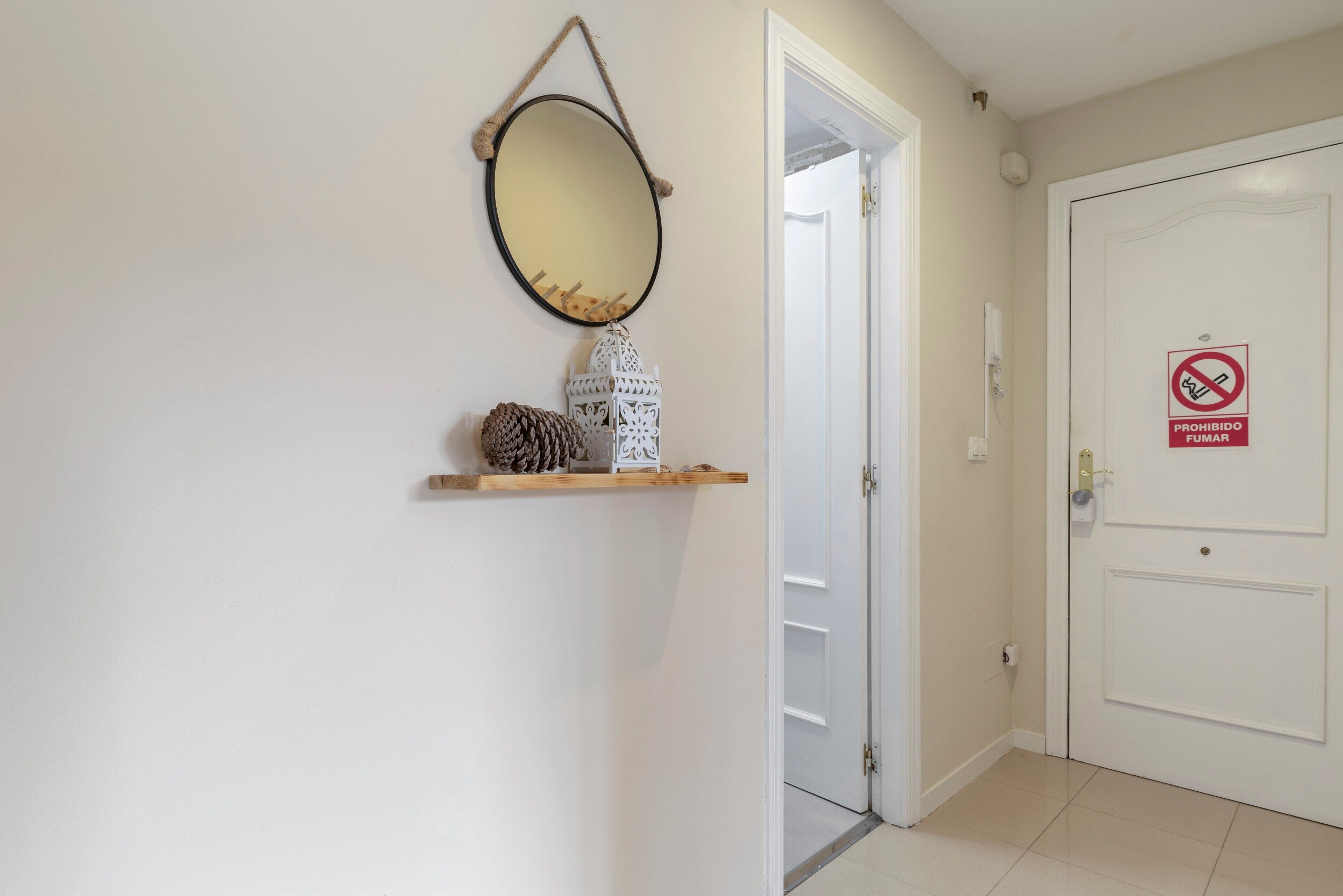A hallway with a white door, a no-smoking sign, and a mirror on the wall.