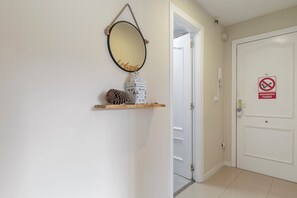 Een gang met een witte deur, een rookvrij sign en een spiegel aan de muur.