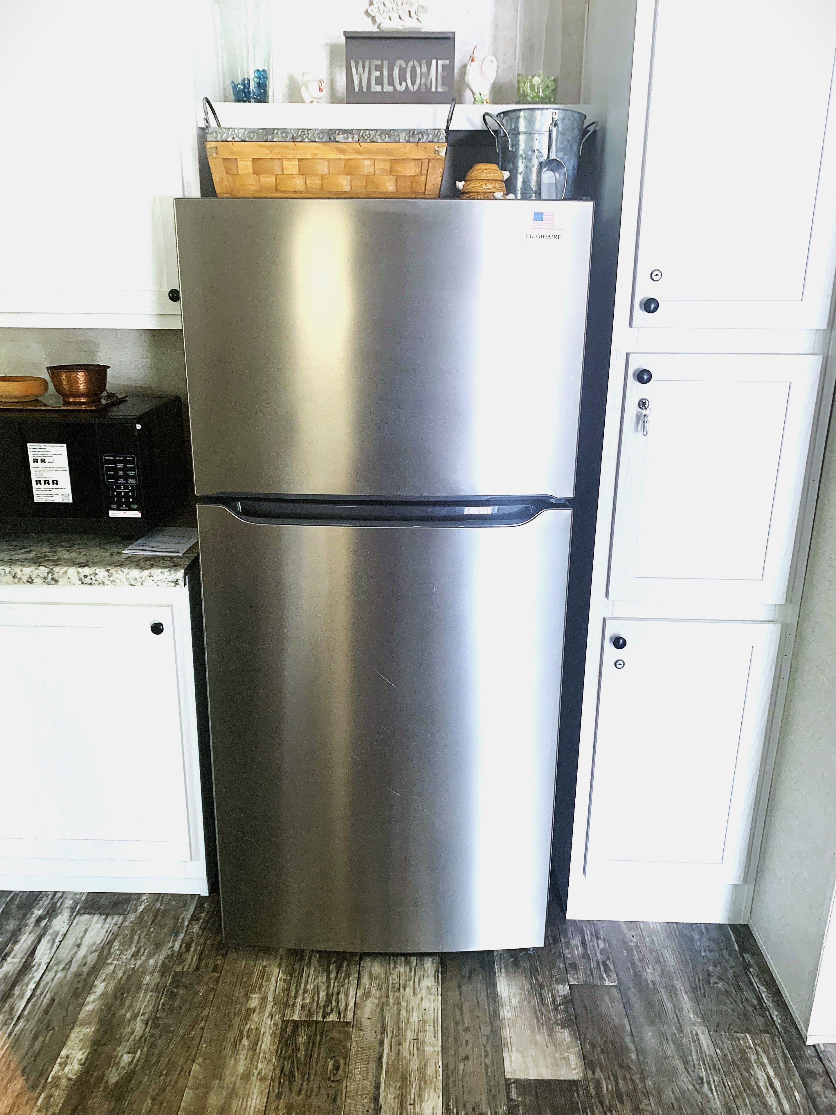 A stainless steel refrigerator in a kitchen with white cabinets and a wooden floor.