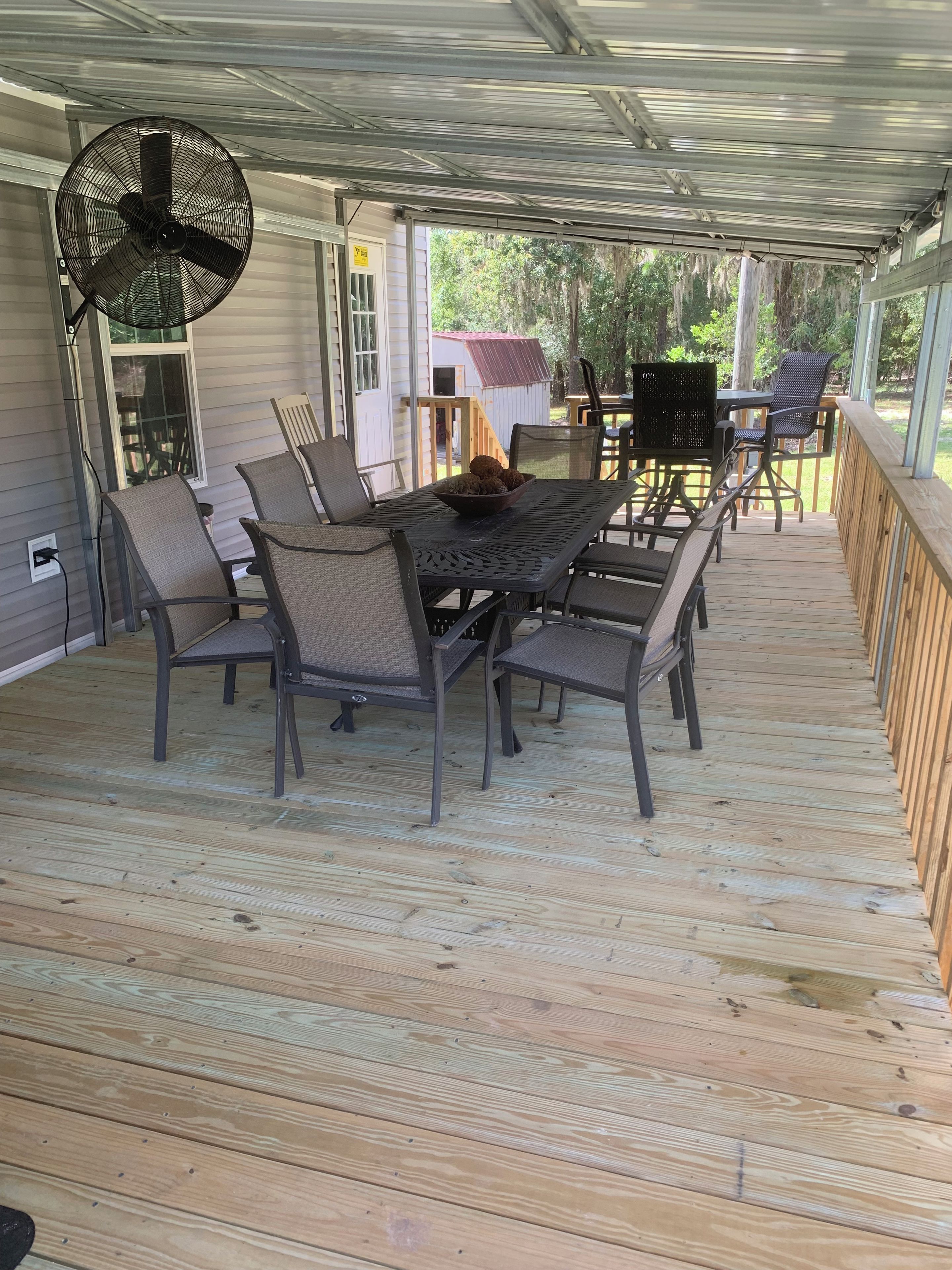 A covered outdoor patio with a table and chairs, a fan, and a view of the surrounding area.