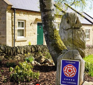 Ein Steinhaus mit einer grünen Tür, einem Baum und einem Schild für VisitEngland Ferienwohnungen.