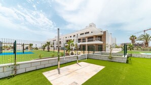 A modern building with a pool, surrounded by a fenced area with artificial grass and a basketball court. - Velapi Golf Resort Oasis, Luxury apartment with golf views, pool and gym by OYOOSTAYS (Los Alcázares)
