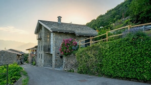 Ein Steinhaus mit Balkon, Blumenkasten mit rosa Blüten und Holzzaun.