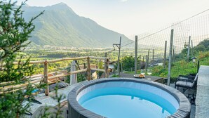 Ein Whirlpool mit Blick auf die Berge, umgeben von einer Holzterrasse und Gartenmöbeln.