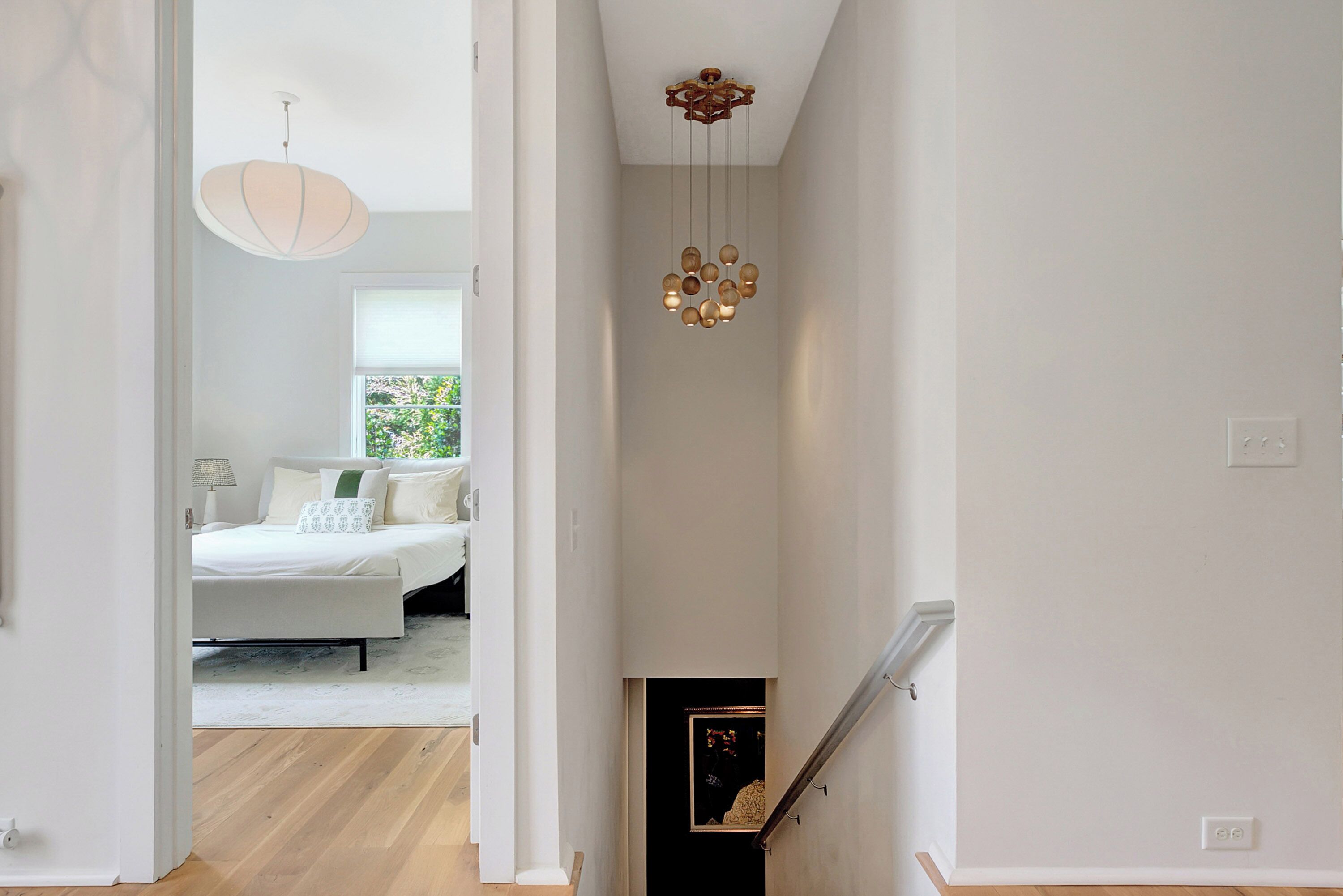 A hallway leading to a bedroom with a bed, a hanging light fixture, and a staircase.