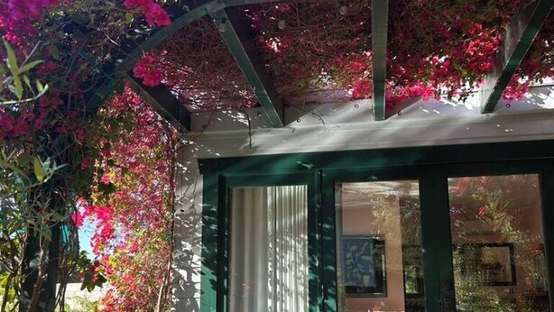 A covered outdoor seating area with a table and chairs, surrounded by lush greenery and flowering plants. - Hollywood Hills Home with Casita: Perfect Multi-Generational Family Compound (Los Angeles)