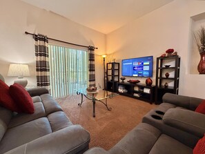 A living room with a sofa, a coffee table, a TV, and a bookshelf. - Ground Floor Condo 4 Pools, Pickleball Near Disney (Davenport FL)
