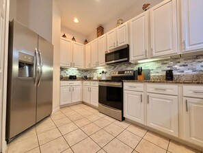 A kitchen with white cabinets, a stainless steel refrigerator, a microwave, and a stove. - Ground Floor Condo 4 Pools, Pickleball Near Disney (Davenport FL)