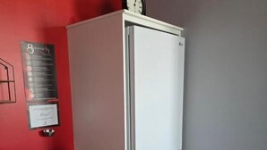 Una habitación compacta con un refrigerador blanco, un escritorio con una silla y un reloj encima del refrigerador.