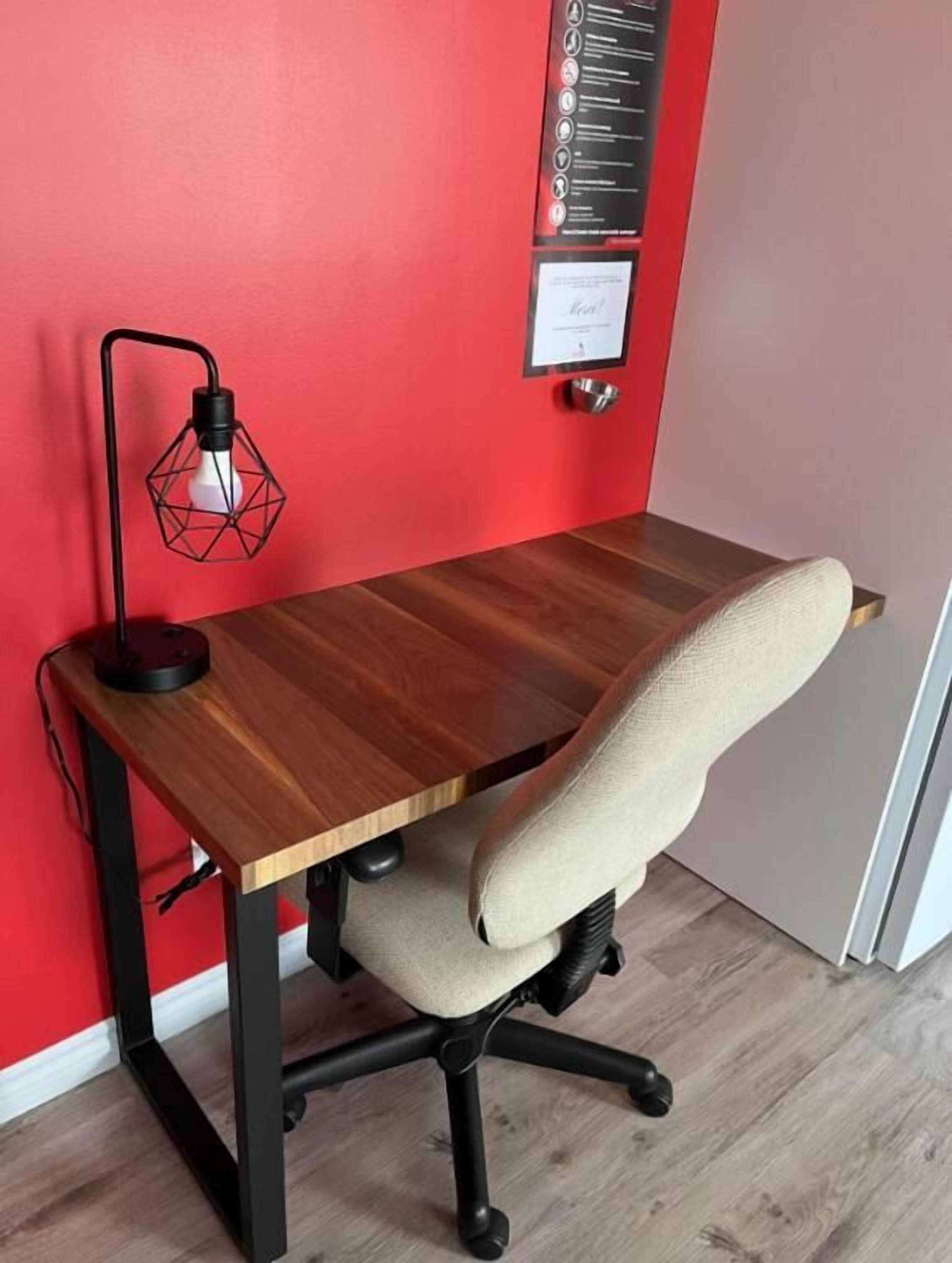 Un bureau en bois avec une chaise, un mur rouge et une lampe noire.