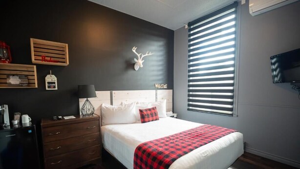 Un dormitorio con cama, cómoda, mesita de noche, televisor montado en la pared y ventana con persianas.