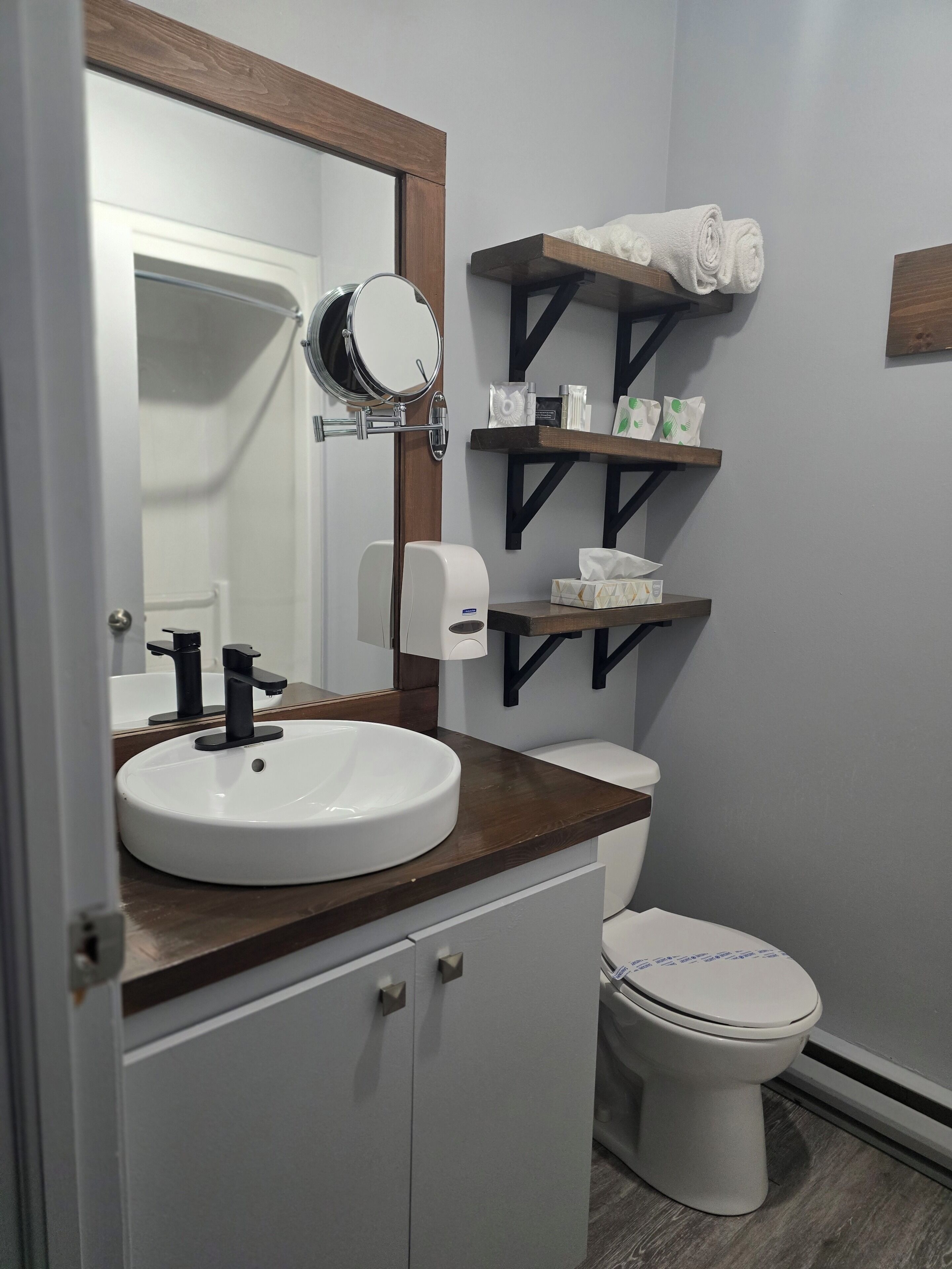 A bathroom with a white sink, a mirror, a toilet, and shelves with toiletries.