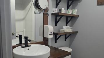 A bathroom with a white sink, a mirror, a toilet, and shelves with toiletries.