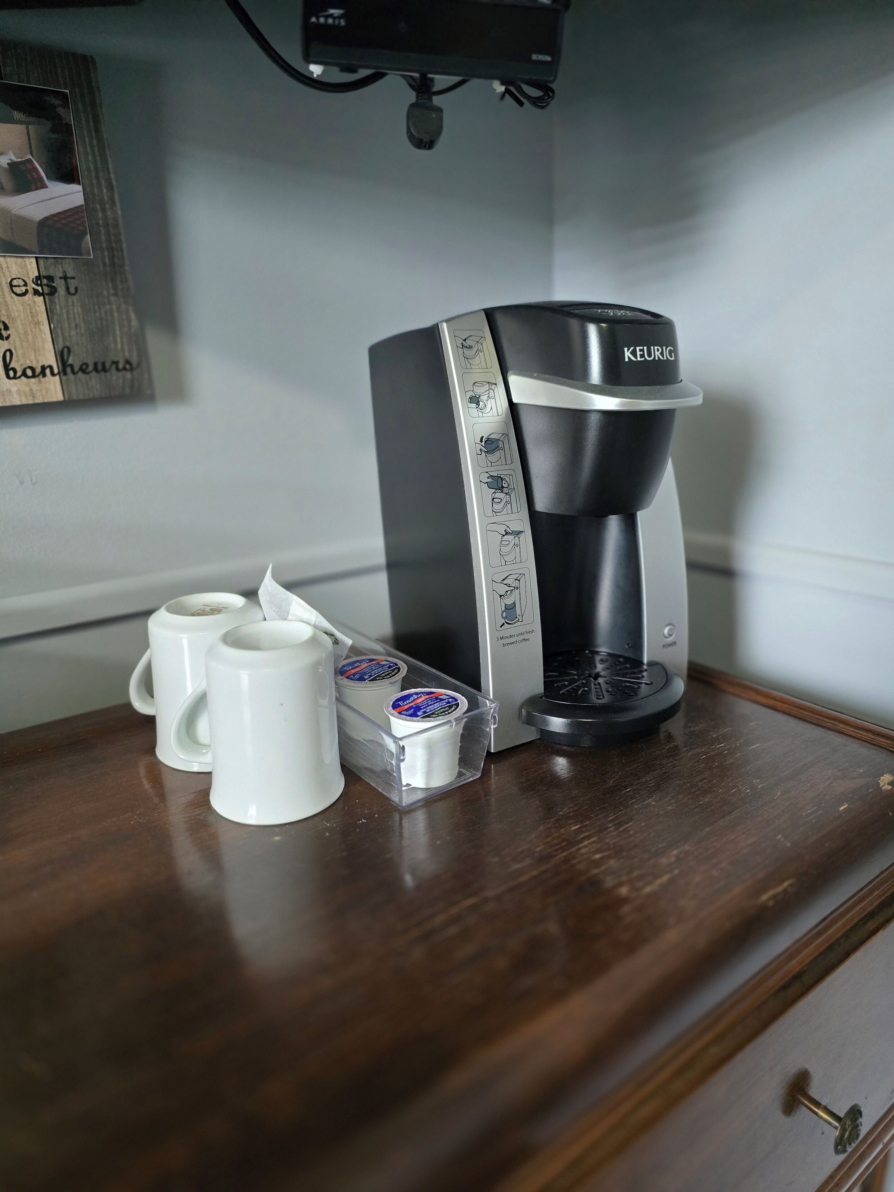 Une machine à café Keurig posée sur une surface en bois, avec deux tasses blanches et deux dosettes de café.