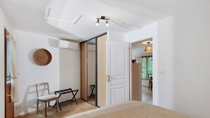A bedroom with a bed, a chair, a small table, a wardrobe, and a door leading to another room.