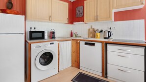 A compact kitchen with wooden cabinets, a microwave, a washing machine, and a dishwasher.