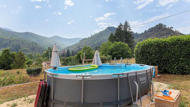 An outdoor swimming pool with inflatable rings, surrounded by a fence, with mountains in the background.