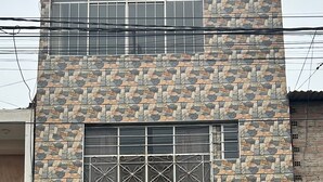 A two-story building with a stone facade, multiple windows with metal grilles, and a visible electrical box on the ground floor.