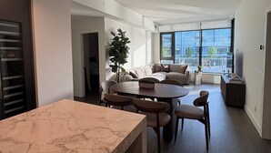 A modern living room with a marble dining table, a sofa set, a large window with a city view, and a potted plant.
