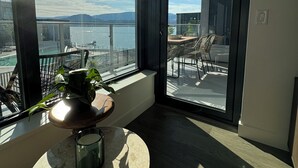 A balcony with a view of a body of water and distant hills, a table with a plant and a candle, and a chair.