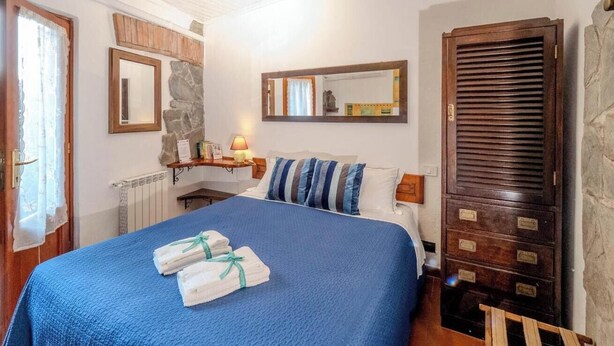 A bedroom with a bed, a nightstand, a mirror, a wardrobe, and a window with curtains.