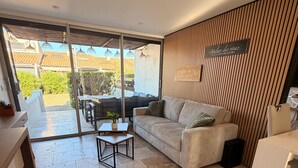 A modern living room with a sofa, a small table, a kitchen area, and a sliding glass door leading to a balcony.
