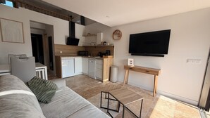A modern living room with a sofa, a dining area with a kitchen, and a TV mounted on the wall.