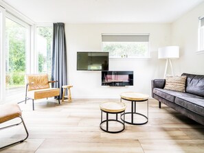 Ein modernes Wohnzimmer mit einer Couch, zwei runden Tischen, einem Fernseher und einem großen Fenster mit Vorhängen.