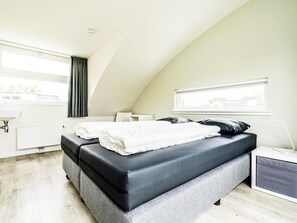 Ein modernes Schlafzimmer mit Schlafbox, Nachttisch, Lampe und einem Fenster mit Vorhängen.