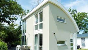 A modern two-story house with a curved roof, large windows, and a patio with outdoor furniture. - Gem With Dune Views for 4 (Vlissingen)