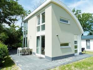 Ein modernes, zweistöckiges Haus mit gewölbter Dachform, großen Fenstern und einer Terrasse mit Gartenmöbeln.