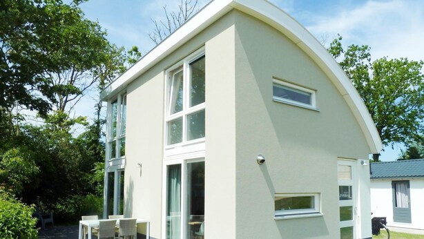 A modern two-story house with a curved roof, large windows, and a patio with outdoor furniture. - Gem With Dune Views for 4 (Vlissingen)
