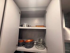 Ein Küchenschrank mit Töpfen, Pfannen und einem Glasbehälter.