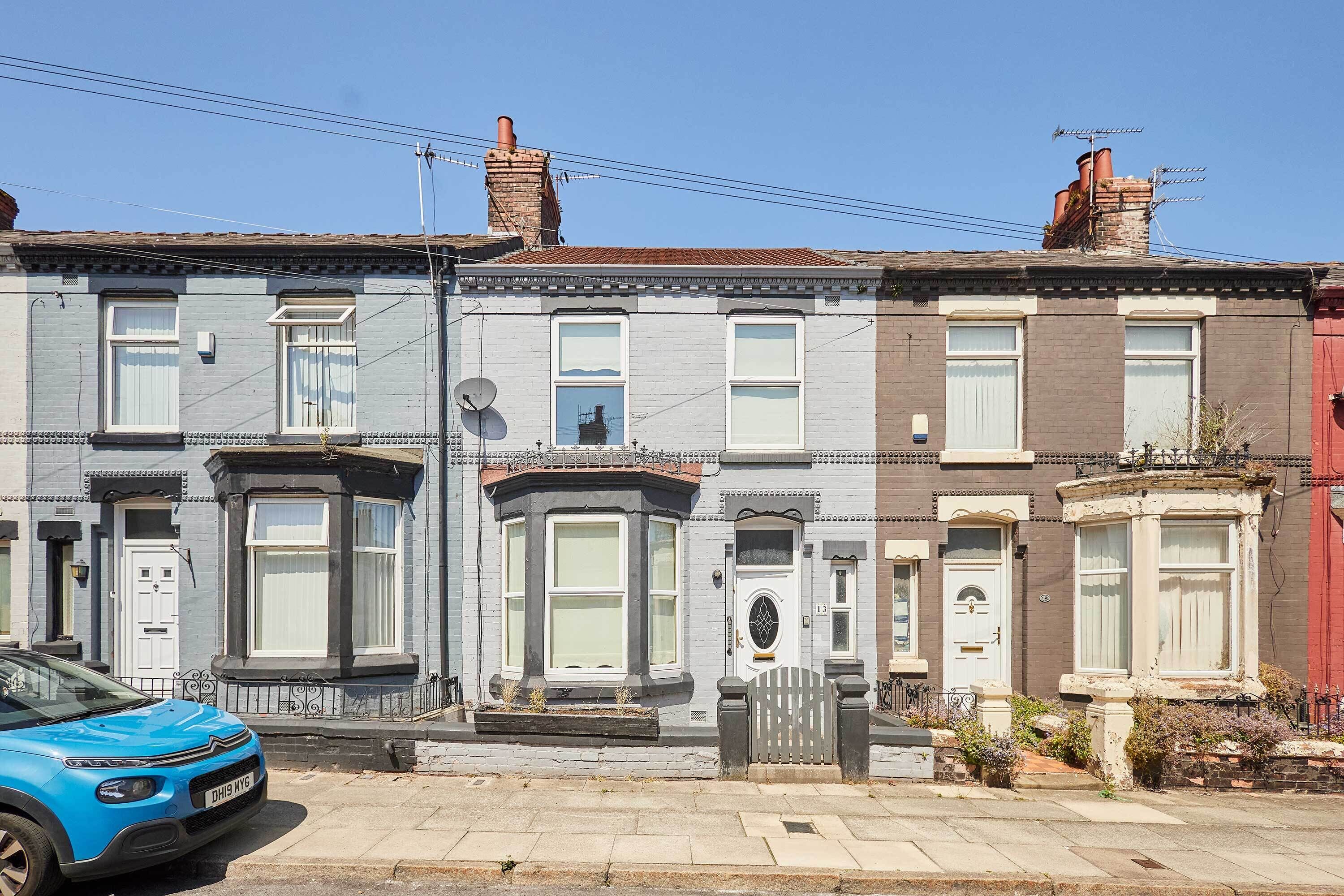 A row of terraced houses with bay windows, a satellite dish, and a blue car parked on the street.