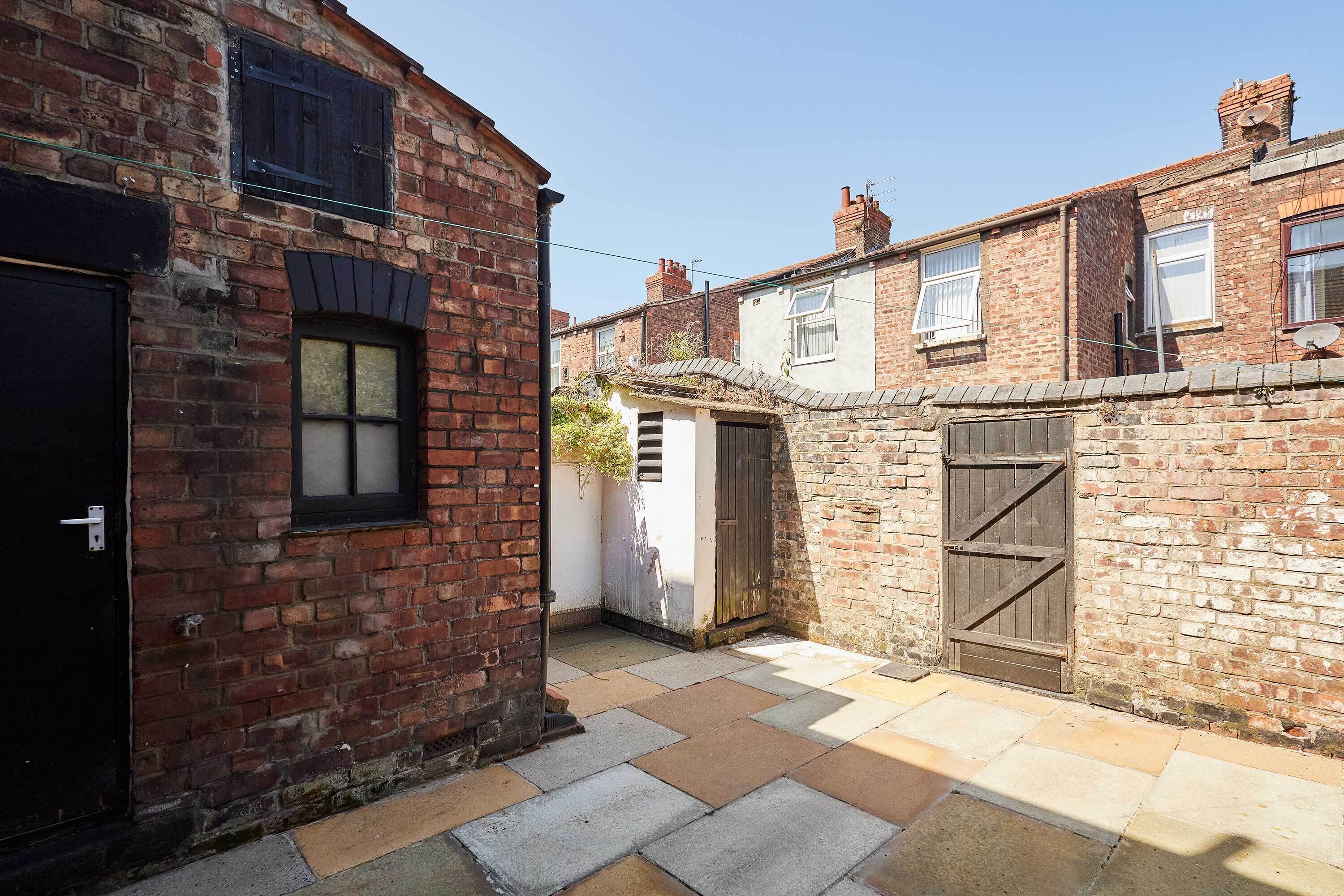 A narrow alleyway with brick buildings, a black door, and a wooden gate.
