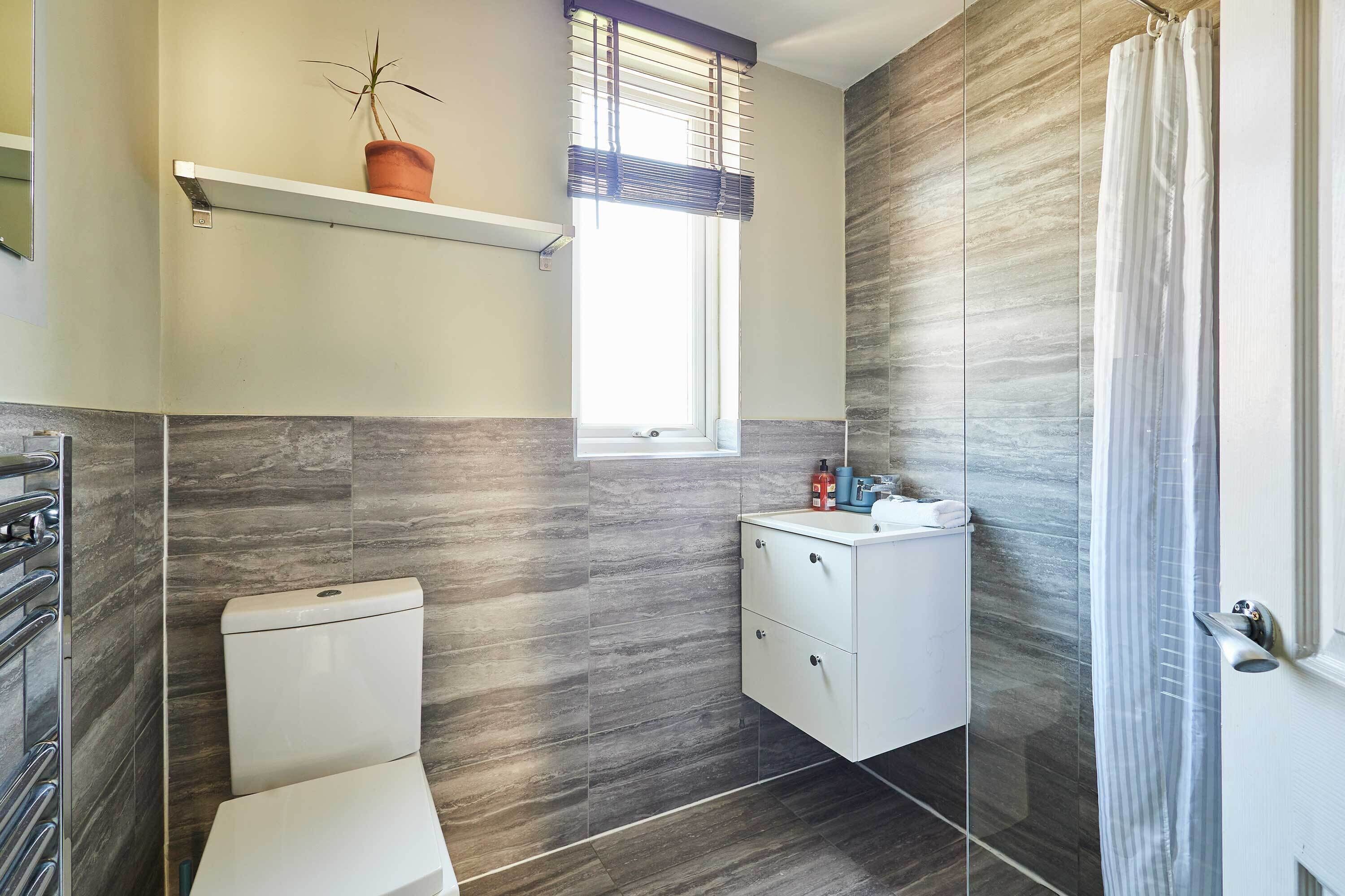 A bathroom with a toilet, a sink, a mirror, a potted plant, and a window with blinds.