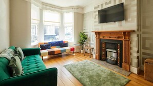 Un salon avec un canapé vert, une cheminée, un téléviseur et de grandes fenêtres.